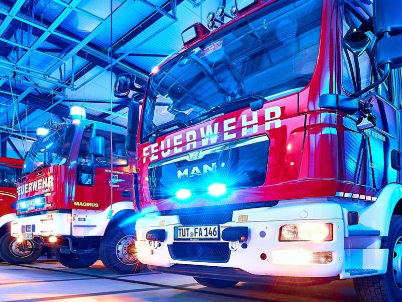 In einer Halle stehen mehrere rote Feuerwehrfahrzeuge nebeneinander, beleuchtet von blauem Licht. Darunter das Kommandantenfahrzeug und HLF 20