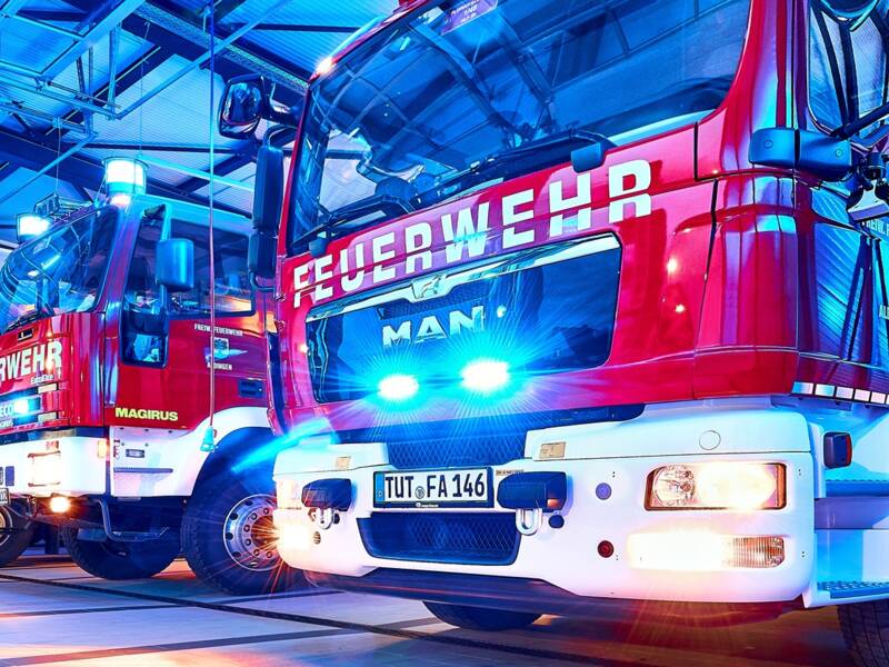 In einer Halle stehen mehrere rote Feuerwehrfahrzeuge nebeneinander, beleuchtet von blauem Licht. Darunter das Kommandantenfahrzeug und HLF 20