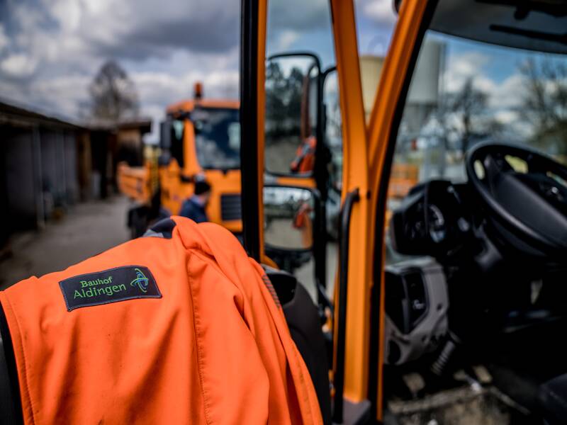 Bild orangene Jacke mit Aufnäher Bauhof Aldingen. Hintergund LKW