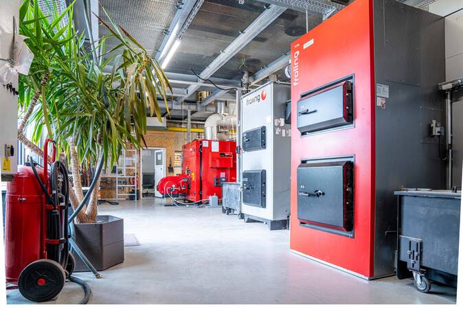 Blick in die Nahwärmezentrale mit zwei Holzhackkesseln im Vordergrund und Spitzenlastkessel im Hintergrund